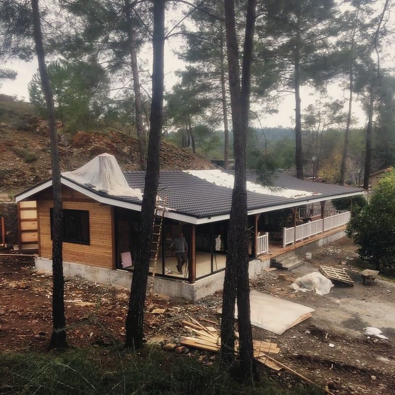 Koyu kiremit çatılı tek katlı ahşap yapı, camlı cephe, beyaz korkuluklu sundurma, çam ormanı