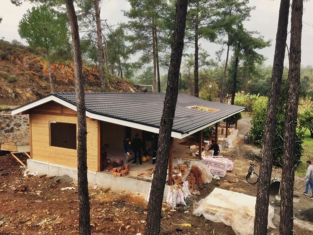 Kiremit çatılı ahşap kaplı yapı, doğramasız pencere boşluğu, sundurma altında tuğla ve yalıtım yığınları