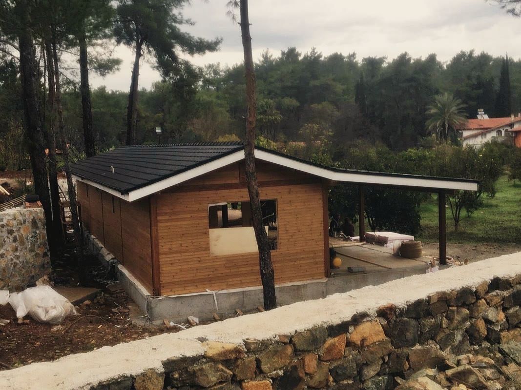 Koyu çatılı ahşap kaplı yapı, doğramasız pencere boşluğu, beton plaklı açık sundurma